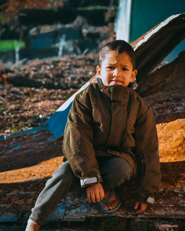 Boy in a brown jacket sitting outdoors